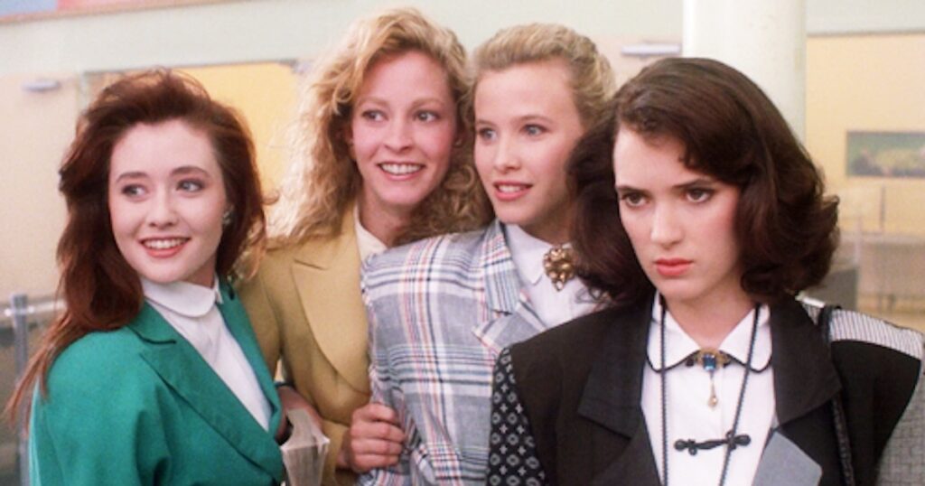 Four actresses from Heathers pose in a variety of 80s blazers with big shoulder pads